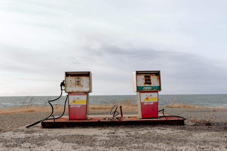 An isolated, weathered gas station with rusting fuel pumps near the ocean shore.