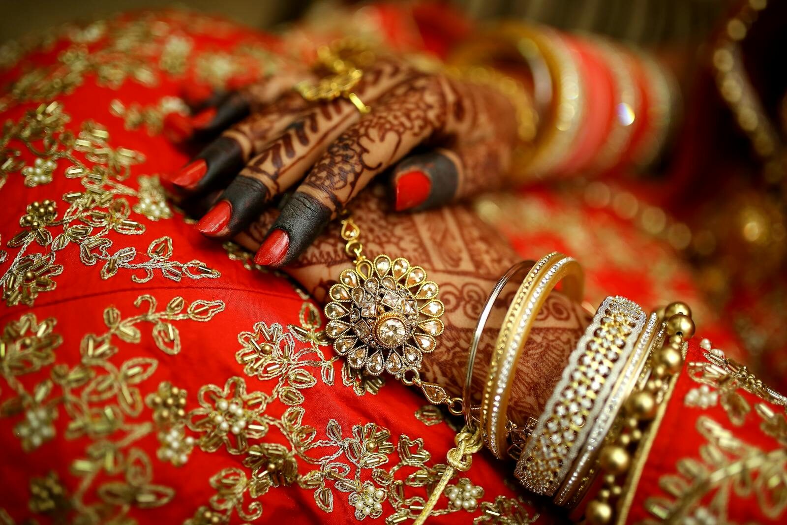 Close-up of ornate henna designs and traditional jewelry on a bride's hands, highlighting Indian wedding elegance.