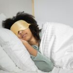 A woman with afro hair sleeps soundly in bed with a sleep mask, enjoying a cozy indoor atmosphere.