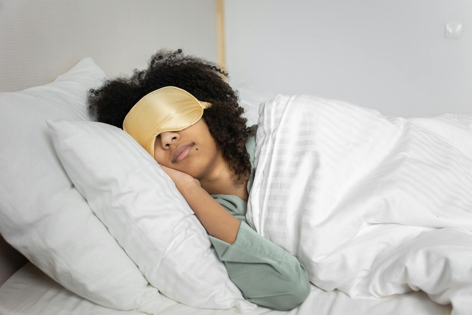 A woman with afro hair sleeps soundly in bed with a sleep mask, enjoying a cozy indoor atmosphere.