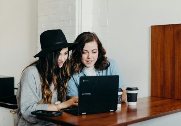 two woman sitting near table using Samsung laptop